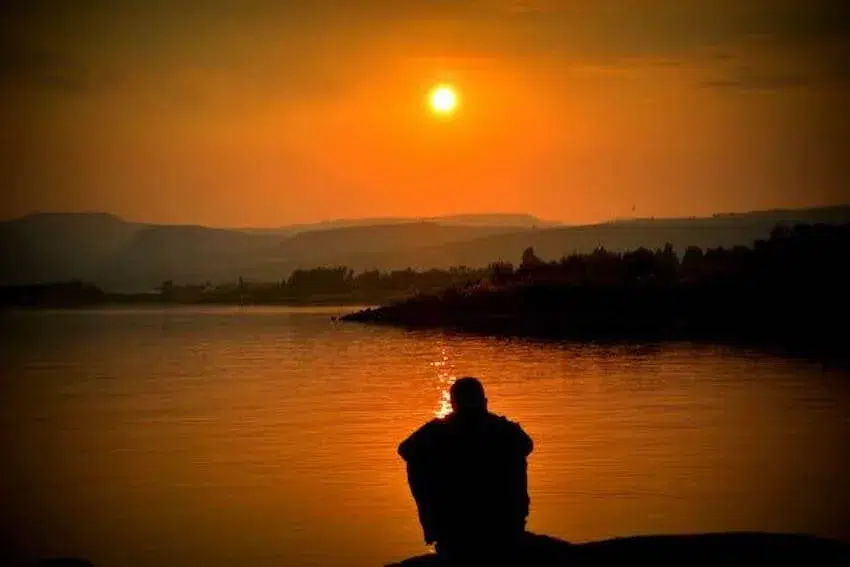 man sitting by the water looking at the sunset