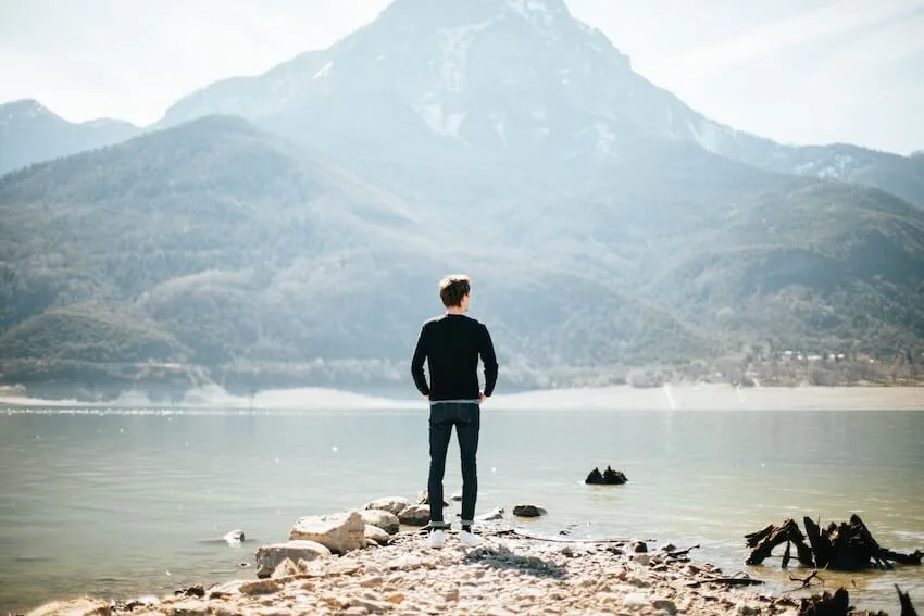 man walking in nature, admiring the view of the water with mountains in the background