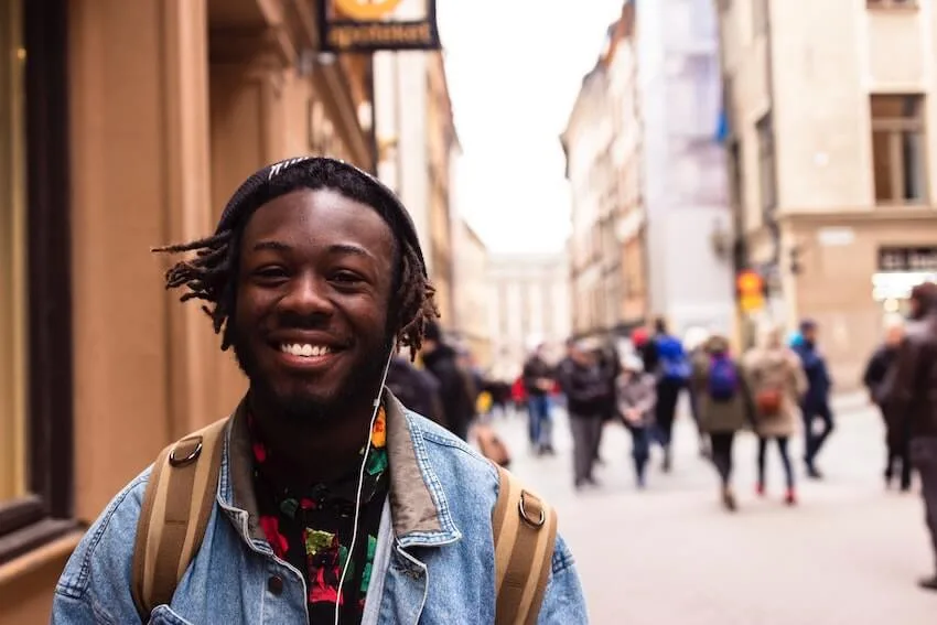 a man smiling while listening to music from his headphones as he walks in a city