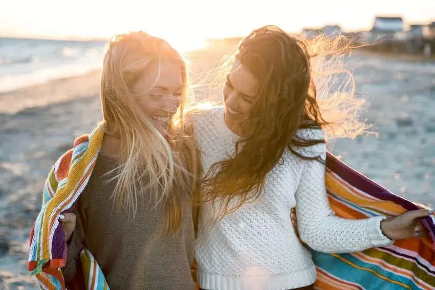two smiling female friends sharing a striped towel over their shoulders
