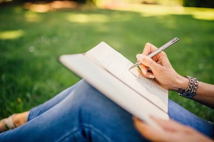 woman sitting on the ground outside writing in her journal