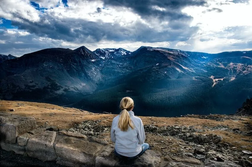 woman sitting outside on the ground admiring the beautiful view of the mountains in front of her