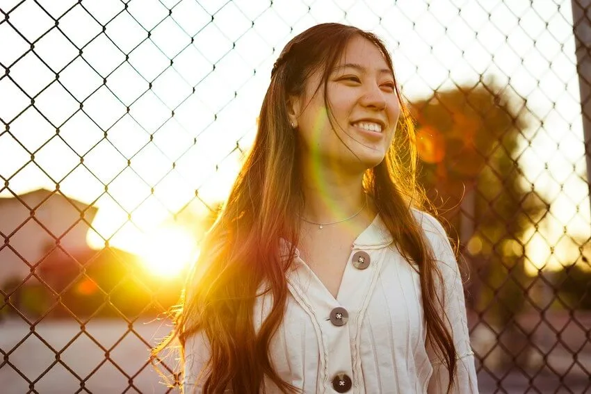 smiling woman standing next to a fence during sunset