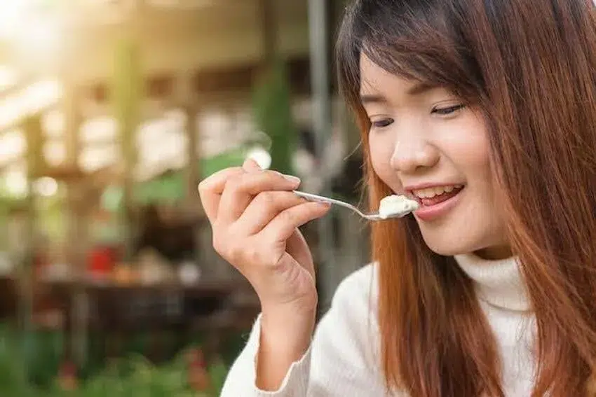 a smiling woman eating a spoonful of ice cream; ice cream is one of her 100 reason to be happy