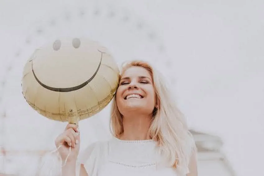 a smiling woman holding a smiley face balloon