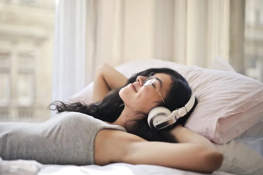 smiling woman listening to happy music while laying in bed