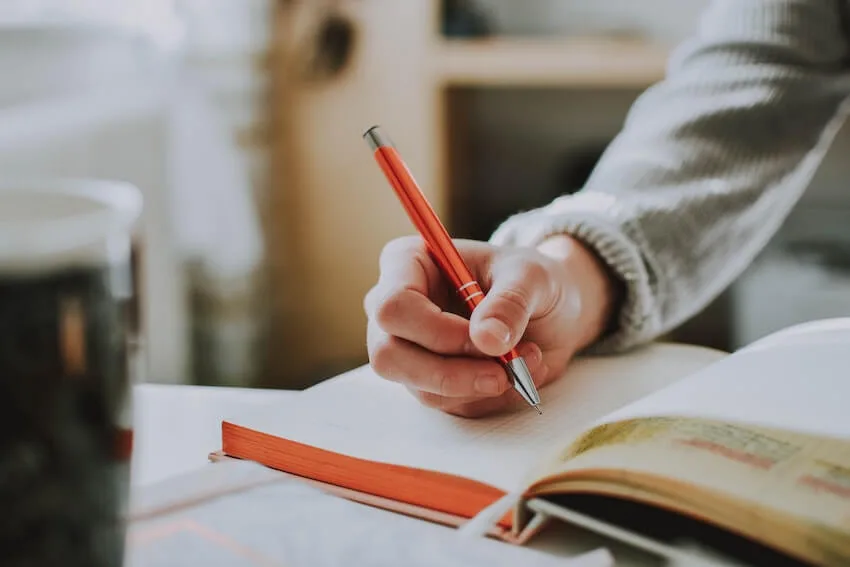person journaling with an orange pen