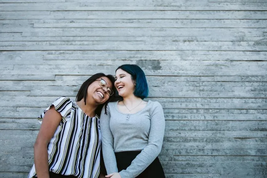 a smiling woman leaning her head on her friend's shoulder