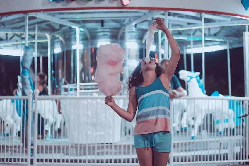 a woman standing in front of a carousel eating cotton candy