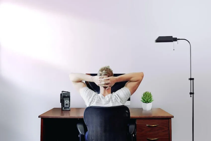 a man sitting at his desk with his hands behind his head, thinking