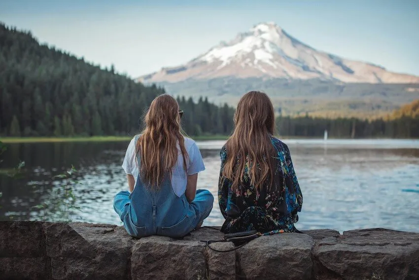 two women sitting and talking at the edge of a lake