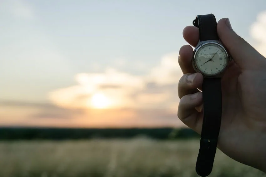 hand holding a wristwatch up with the sunset in the background