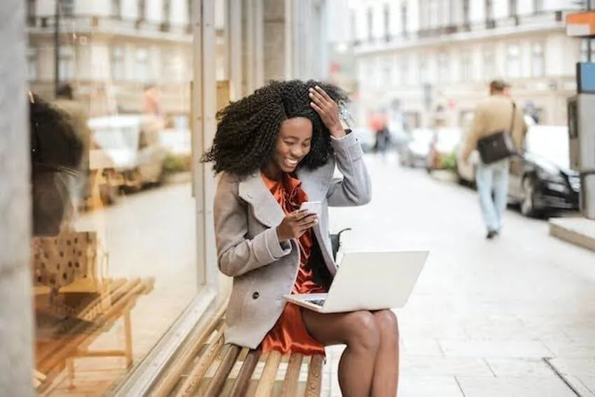 Woman sitting on a bench outside smiling at her phone