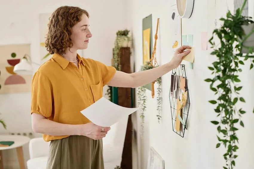woman in an orange shirt creating a vision board on her wall