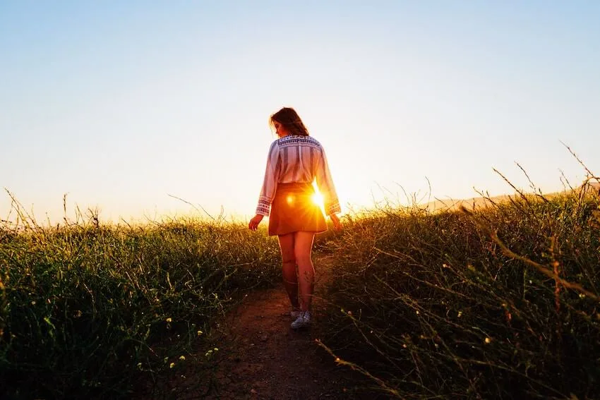 woman walking through a field at sunset
