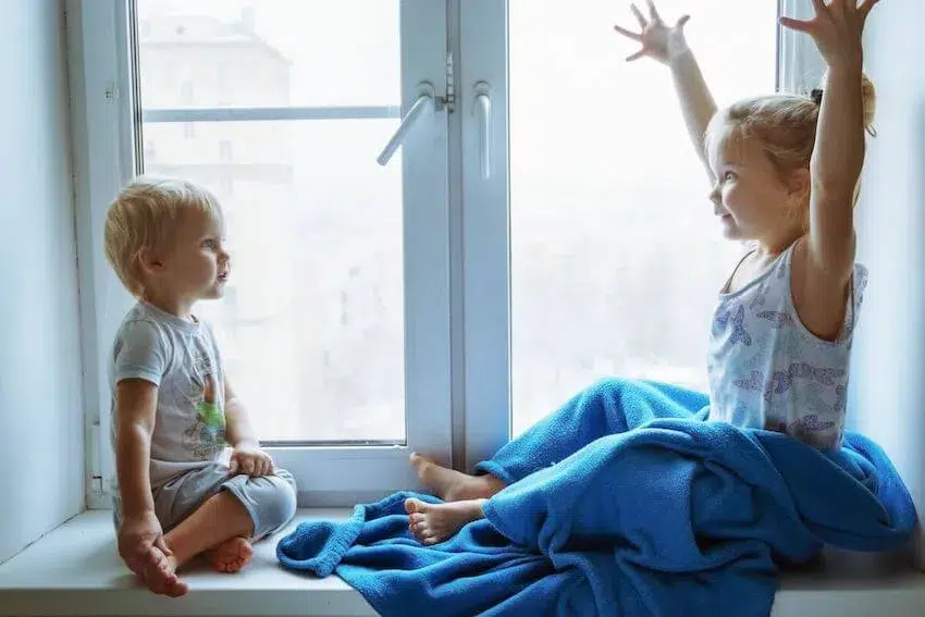 a little girl with her arms raised up above her head with her fingers spread wide, telling a little boy a story