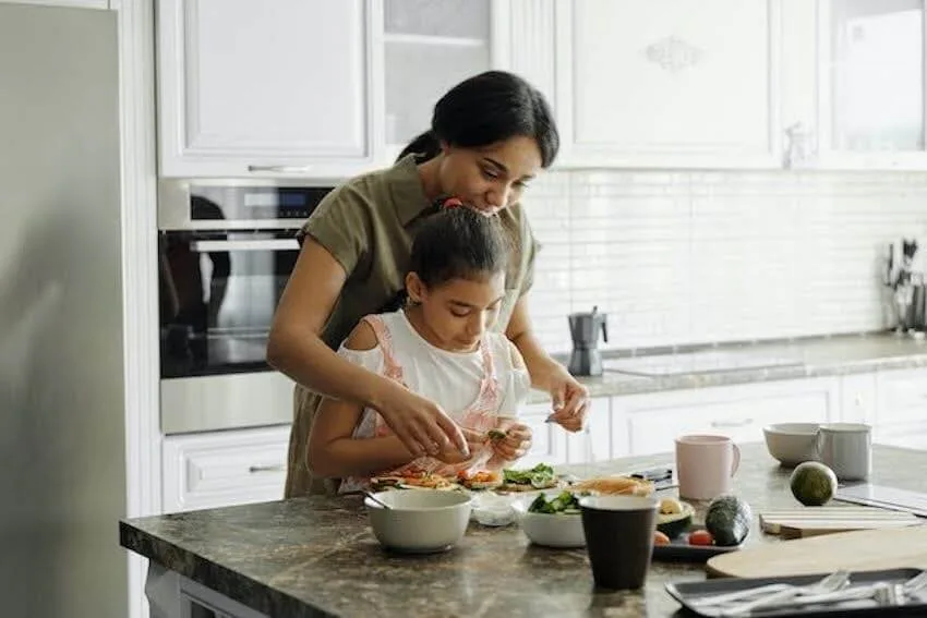 a woman helping her young daughter prepare a meal