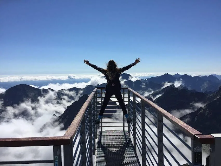 woman standing high up over the mountains with her arms up