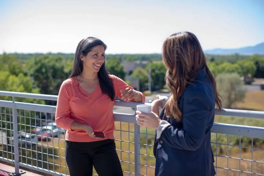 two women standing next to a fence having a good conversation