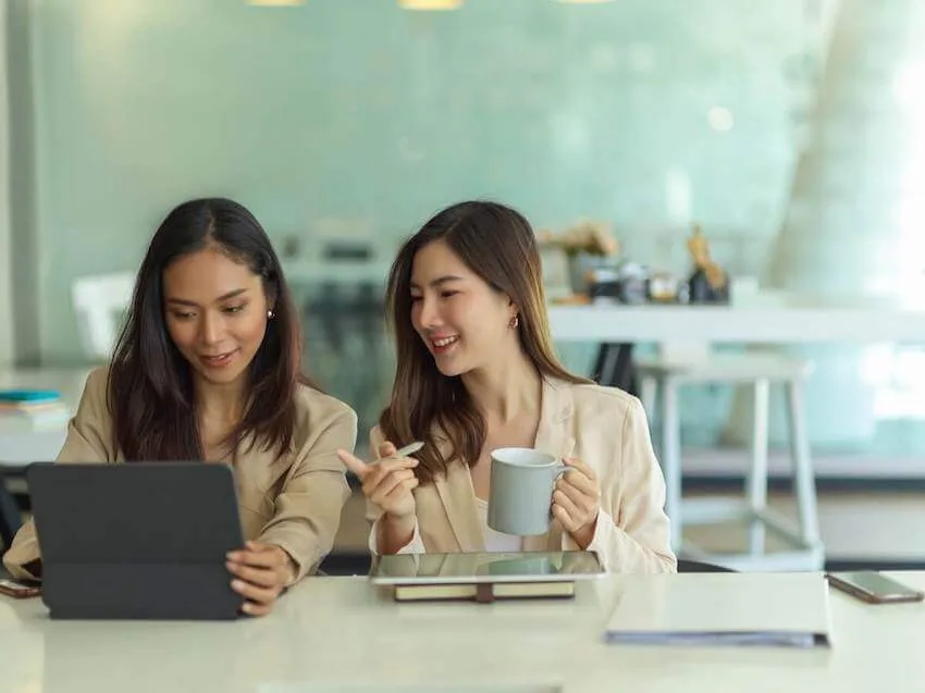 two women smiling while looking at a tablet